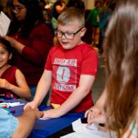Students laugh as they get their paper passports stamped at a table at student project showcase
